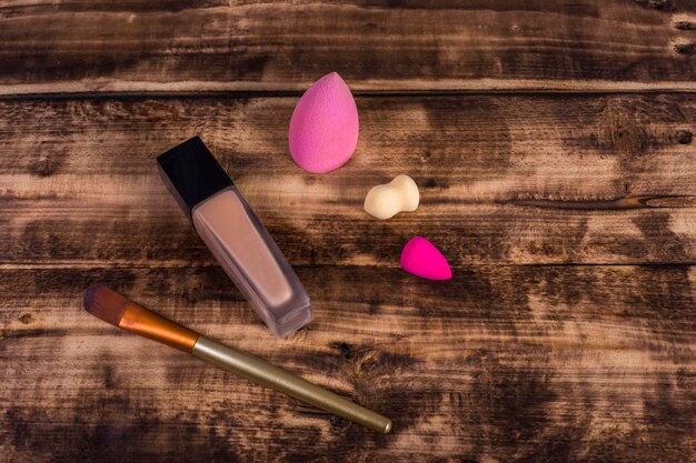 A selection of makeup products including concealer, foundation, and a makeup sponge, neatly arranged on a wooden surface, highlighting their textures and colors.