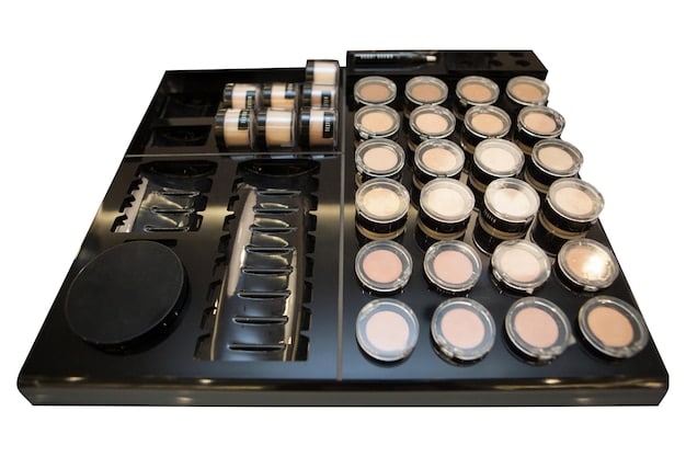 A series of male makeup products displayed on a sleek, minimalist shelf. The products include tinted moisturizers, concealer sticks, eyebrow gels, and a small eyeshadow palette with neutral tones.