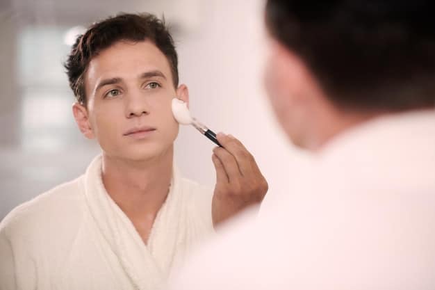 A man applying concealer under his eyes in a well-lit bathroom. The focus is on his hands and the product, showcasing the practical application of makeup.