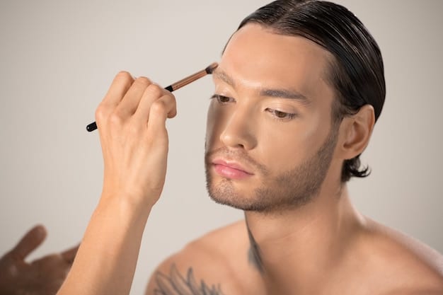 Close-up of a man's hands applying concealer under his eyes with a small brush. The lighting is soft and natural, highlighting the texture of the skin and the makeup product. Clean background.