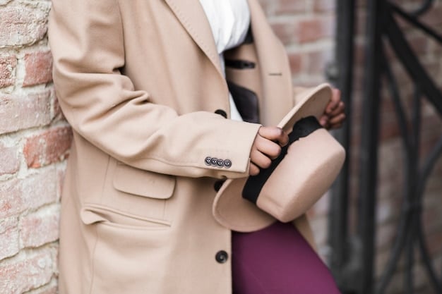 A close-up shot of an outfit featuring a beige unisex oversized blazer paired with a black turtleneck sweater, dark wash straight-leg jeans, and black Chelsea boots. The individual is standing in front of a minimalist background, highlighting the outfit's simple yet stylish combination.