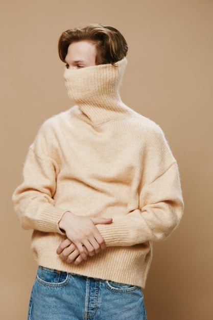 A person wearing a layered outfit: a thin grey turtleneck, a chunky beige knit sweater, a dark denim jacket, and a black scarf, showcasing a stylish and practical layering combination.