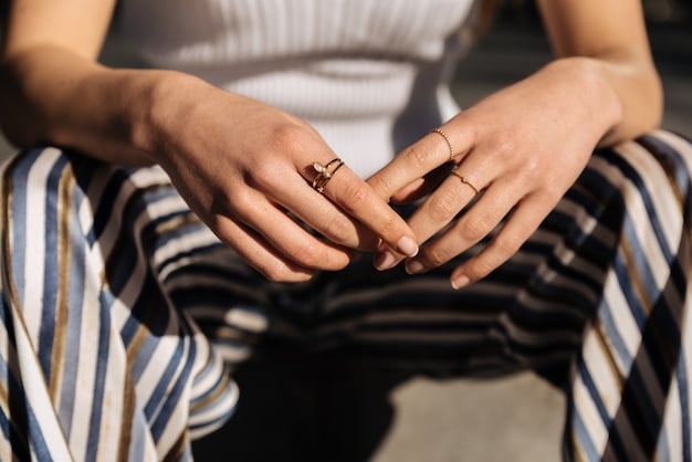 Close-up shot of a person's hands adorned with various rings, including signet rings, minimalist bands, and gemstone rings. The person is wearing a neutral-colored outfit, highlighting the jewelry.