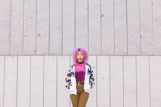 A non-binary person is captured from the waist up, showcasing a stylish outfit featuring a mustard yellow t-shirt and a lavender blazer. They are standing in front of a vibrant, graffiti-covered wall.