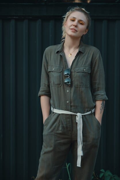 A person wearing a belt over a jumpsuit, cinching at the waist to create a more defined silhouette. The belt is stylish and bold, adding a unique element to the outfit. The background is a blurred, upscale boutique setting.