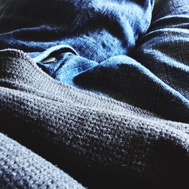 A close-up shot of different fabric textures layered together, including wool, silk, and denim. The textures are juxtaposed to create a visually interesting and androgynous look.