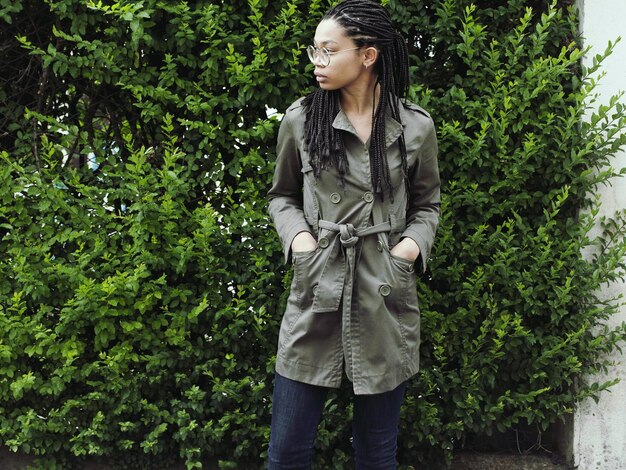 A person wearing a long, flowing trench coat in a neutral color, layered over a simple outfit. The trench coat is designed to be gender-neutral and versatile.