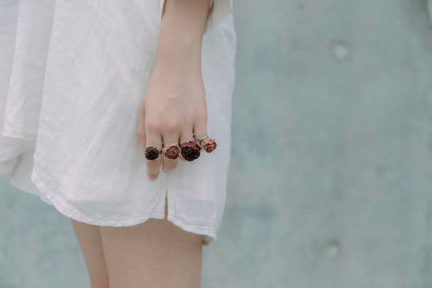 A close-up of hands wearing a variety of rings in different metals and styles, showcasing both delicate and bold designs. The background is a soft, neutral fabric.