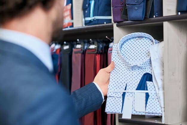 A close-up of a hand selecting a navy blue blazer from a well-organized closet filled with androgynous workwear staples, including button-down shirts, dress pants, and neutral-colored sweaters.