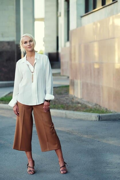 A person wearing a flowy, oversized button-down shirt with wide-leg trousers, accessorized with minimalist jewelry. The outfit is loose-fitting and comfortable, showcasing a relaxed androgynous silhouette.