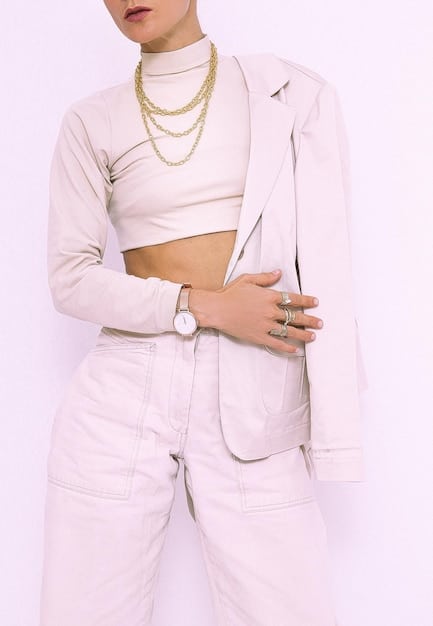 A close-up shot of a person wearing a crisp white button-down shirt with rolled-up sleeves, paired with a loosely fitted blazer in a muted earth tone and subtle jewelry.