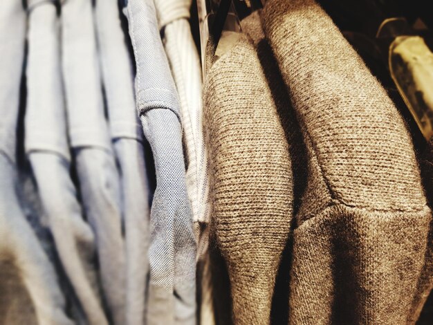A close-up shot of a rack of clothing featuring a mix of neutral and versatile pieces such as plain t-shirts, button-down shirts, and straight-leg jeans in various sizes and colors. The focus is on the texture and fabric of the clothing, highlighting quality affordable basics.