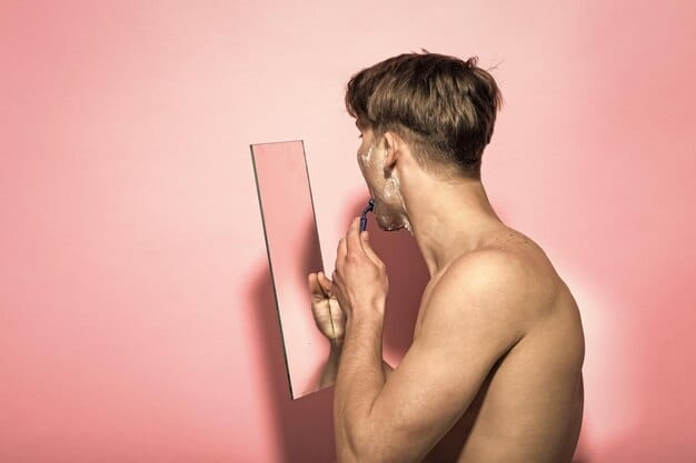 A man holding up three different shades of concealer to his jawline in natural light, comparing the shades to find the best match. He is looking in a mirror with a critical eye, assessing the blend.