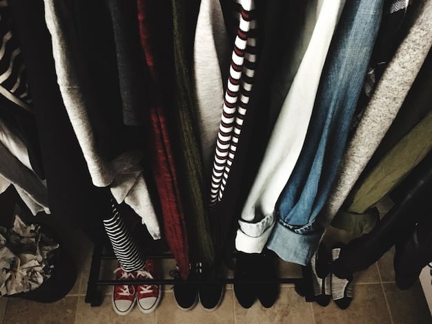 A closet organized with unisex clothing items, including trench coats, denim jackets, sweaters, and trousers in neutral colors. The organization is minimalist and functional.