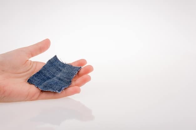 A close-up shot of a person's hands performing a meticulous double roll on the hem of a pair of dark wash unisex jeans, emphasizing the neat folds and texture.