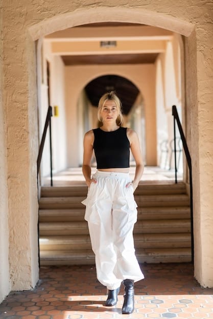 A person in a sleek black unisex t-shirt, French-tucked into crisp white wide-leg trousers, wearing minimalist gold layered necklaces and a structured black leather shoulder bag, walking confidently in a bright, modern setting, epitomizing minimalist chic.
