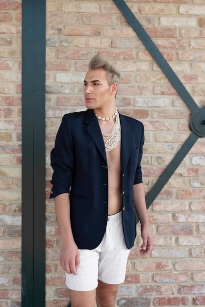 A non-binary person wearing an oversized navy blazer over a crisp white button-down shirt, paired with tailored black trousers and black loafers. They are accessorized with a thin silver necklace and a classic watch.