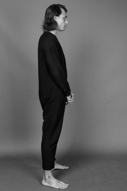 A person from the waist down, standing on a textured grey surface, wearing black wide-leg trousers and white sneakers. The trousers are slightly cropped, revealing a glimpse of patterned socks. The lighting is natural and soft, highlighting the drape of the fabric.