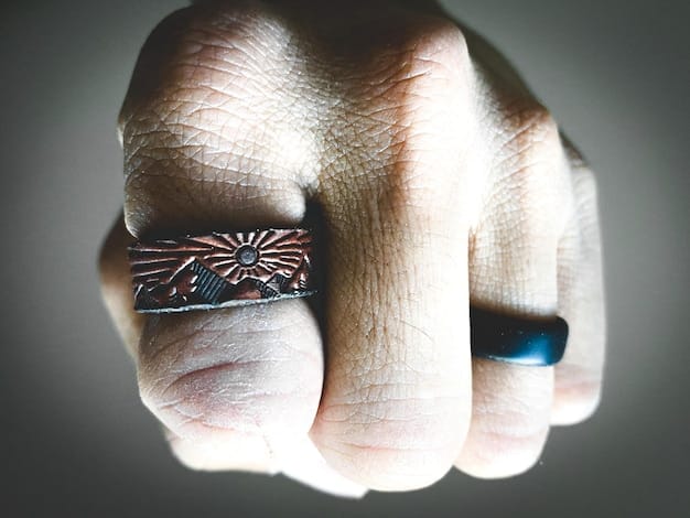 Close-up of a collection of gender-neutral rings, stacked on a hand, with different textures and metal finishes. The background is soft and blurred, highlighting the details of the rings.