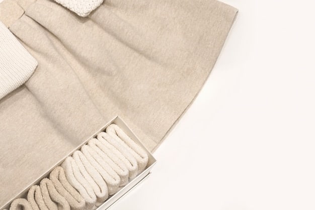 A close-up shot showcasing a neatly folded pile of neutral-colored clothing items, including a white button-down shirt, a gray crew-neck sweater, a black blazer, and a pair of dark wash jeans. The image emphasizes the texture and quality of the fabrics, communicating versatility and style.