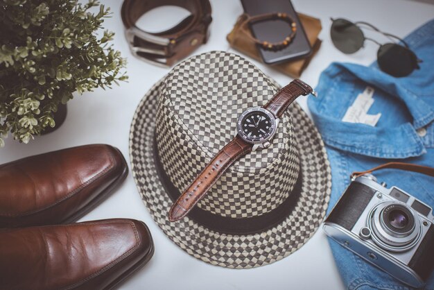 A close-up of androgynous accessories laid out on a table, featuring a mix of items like a fedora, a minimalist watch, a leather belt, and a pair of classic sunglasses.
