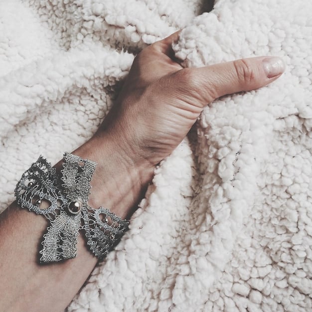 A close-up shot of hands adorned with geometric rings and bracelets in silver and gold, showcasing various androgynous jewelry pieces. The background is a soft, neutral fabric.