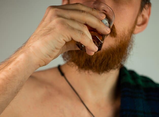 A person's hand holding an opened bottle of beard oil, peering closely at the oil's consistency and color, possibly trying to smell it.