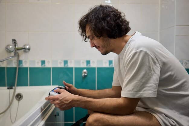 A man in a modern and well-lit bathroom, applying a small stripe of foundation along his jawline using his finger, with multiple other foundation bottles open beside him, suggesting choice and careful testing.