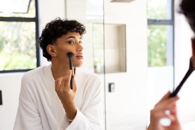 A man with a deep, warm skin tone applying a rich, terracotta red lipstick, his expression confident and stylish. The setting is clean and modern.