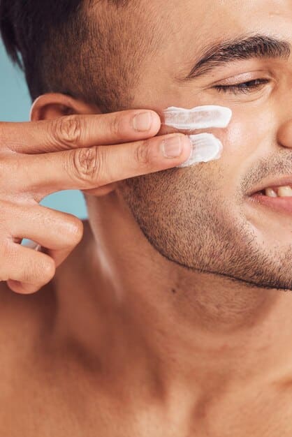 A detailed close-up of a man's finger applying a small amount of sunscreen below his eye, emphasizing sun protection.