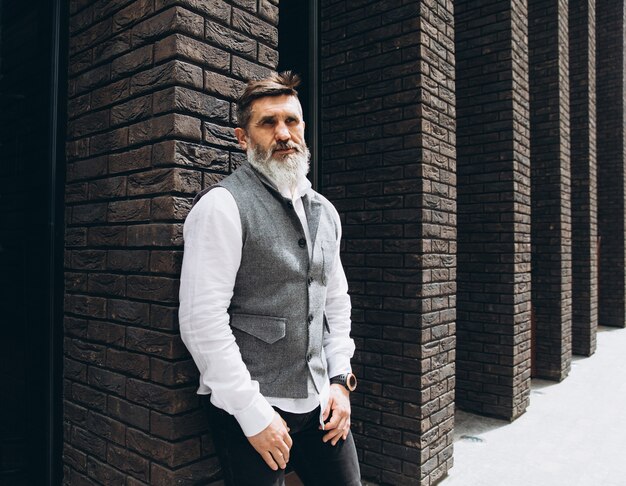 A stylish American man with a well-groomed, medium-length full beard that is neatly shaped, standing confidently in a professional setting.