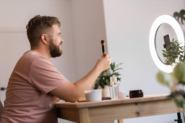 A male influencer demonstrating a simple, natural makeup routine for camera, showing how to even skin tone and define features with gender-neutral products. The setting is bright and aspirational.