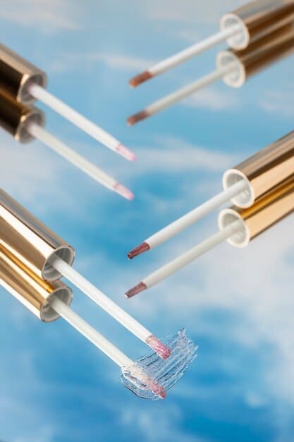 A close-up of various modern, sleek lip gloss tubes and applicators arranged aesthetically on a smooth, reflective surface, showcasing different subtle tints and highlighting their innovative design.