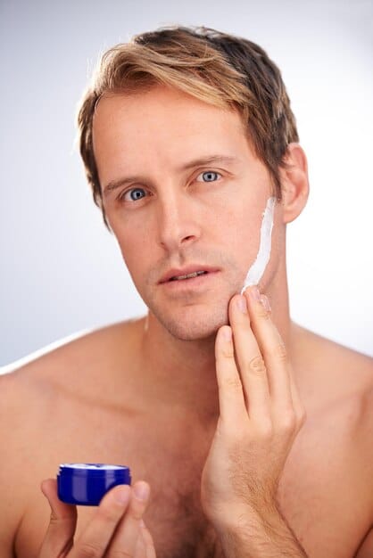 A man gently dabbing BB cream onto his cheek with his fingertips, emphasizing natural application and texture.