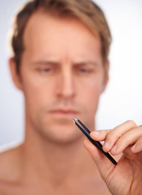 A man's hand correcting a small mistake on his eyebrow with a cotton swab after applying brow gel, illustrating the need for precision and correction in grooming