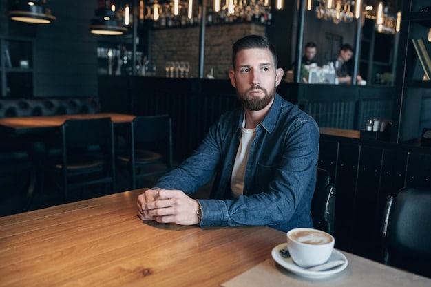 A man sitting at a restaurant table in the evening, wearing a business casual outfit. He has a light-colored chino pants, a navy blue button-down shirt, and brown leather shoes. The soft lighting of the restaurant enhances the relaxed and stylish vibe of the outfit, exemplifying From Desk to Dinner: 3 Men's Style Outfits That Transition Seamlessly.