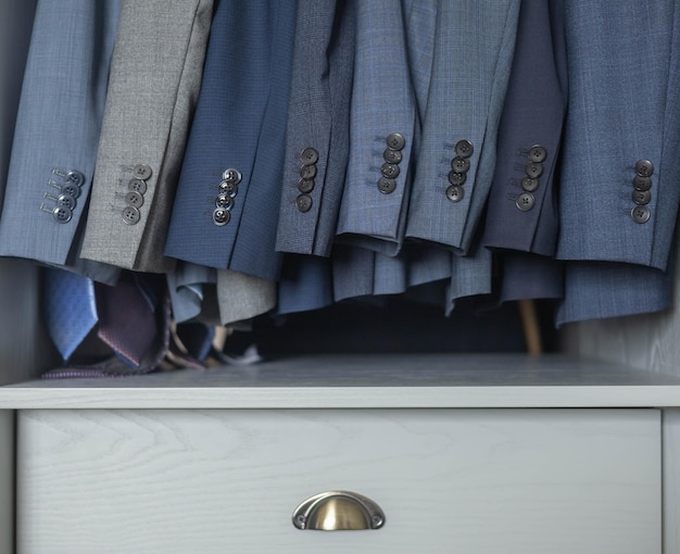 A close-up shot of various classic items in a men's wardrobe, including a navy blazer, white dress shirt, tailored trousers, and leather shoes. The focus is on the texture and quality of the materials, illustrating the concept of investing in timeless pieces as one of the 5 Men's Style Resolutions to Make in 2025.
