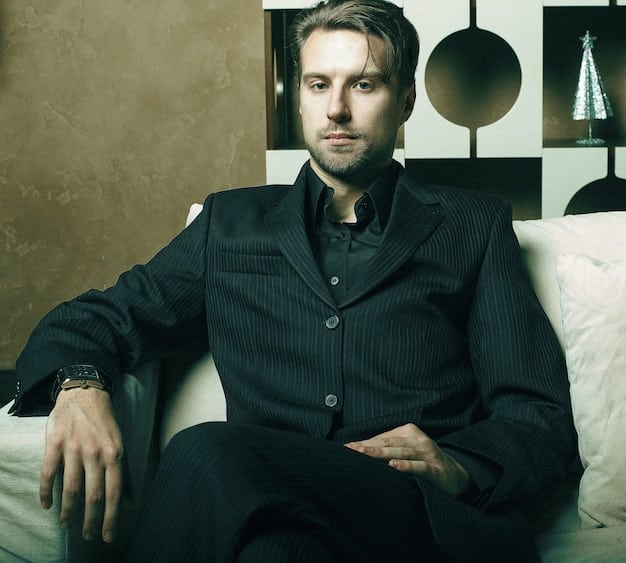 A visually striking image of a man in his late 20s, dressed in modern, minimalist attire, applying cologne to his neck. The background is a blurred urban landscape, suggesting a cosmopolitan lifestyle. The focus is on the action of applying the fragrance, highlighting its role in personal grooming and style. This is relevant to Men's Fragrance Trends: What Scents Will Be Most Popular in 2025?.