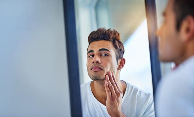 A man checking his reflection in a mirror, subtly smiling and appearing confident. His eyebrows are neatly styled and defined, showcasing the natural look achieved with brow gel. The image conveys the positive impact of grooming on self-esteem and appearance.