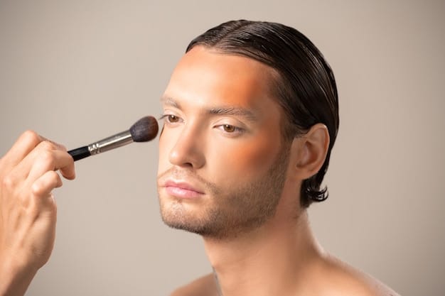 A man using a flat-top kabuki brush to apply liquid foundation to his cheek, demonstrating a seamless and natural makeup application technique.